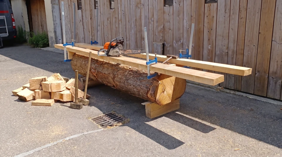 Sciage en extérieur d'un tronc d'arbre écorcé sur tréteaux en bois
